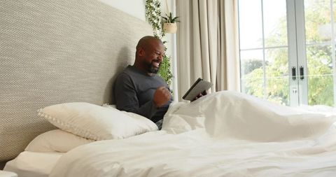 Happy Man Celebrating on Bed Using Tablet