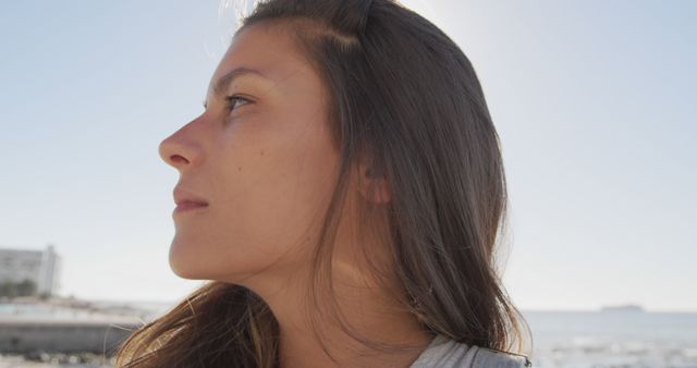 Young woman with long hair gazing at the ocean on bright sunny day. Ideal for themes of contemplation, peacefulness, and nature appreciation. Useful for articles on mindfulness, mental health, travel blogs, and personal growth stories.