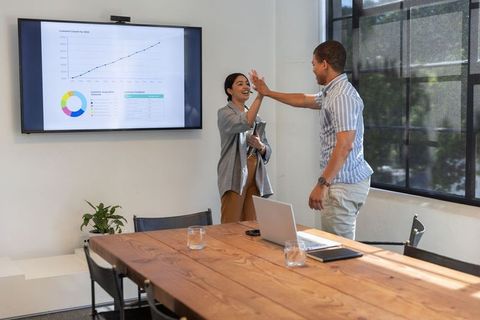 Diverse colleagues celebrating successful presentation in modern office