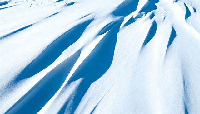Wind-Sculpted Snow Drifts on Alpine Ridge with Deep Blue Shadows and Smooth Cornices