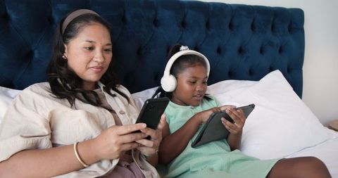 Diverse Mother and Daughter Bonding over Technology in Cozy Bedroom
