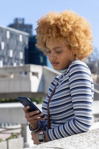 African american woman leaning on plaza rail checking smartphone in urban striped top