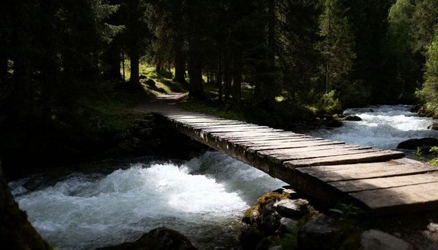 Rustic wooden footbridge crossing rushing mountain stream in shaded forest