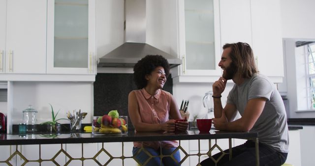 Young couple enjoying morning coffee while having a friendly chat in a modern kitchen setting. The cheerful interaction highlights warmth and togetherness, making it perfect for content related to family, relationships, home decor, and everyday lifestyle. The scene can also promote kitchen appliances, home goods, and breakfast products.