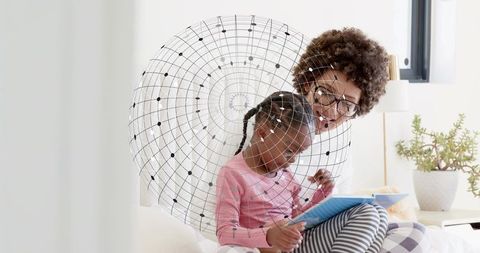 Caregiver guiding child reading tablet on sunlit couch, nurturing digital learning