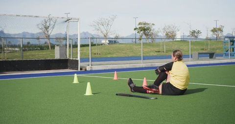 Female Athlete Resting on Field Hockey Turf Near Equipment