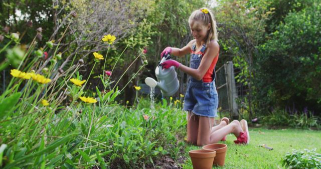 Young girl kneeling in a lush garden, watering plants with a watering can. Bright yellow and pink flowers visible in foreground. She wears denim overalls and a red sleeveless top, summery vibe enhanced with a headband. Perfect for use in articles about children's activities, outdoor fun, gardening tips, and healthy lifestyles.