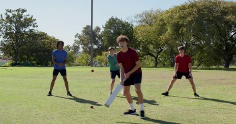 Multiracial youth team playing cricket on sunny park field practicing batting and fielding