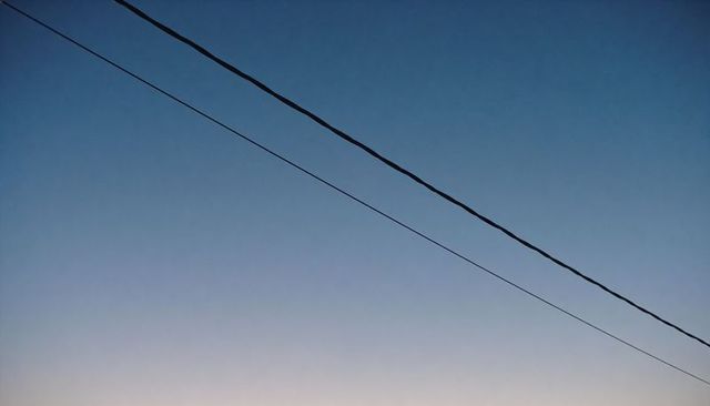 Diagonal utility wires crossing calm blue dawn sky with soft pastel gradient minimalism
