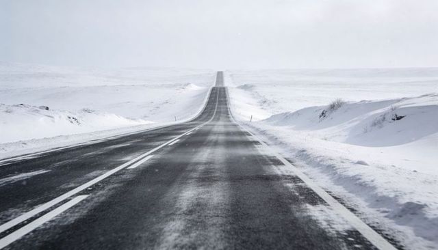 Endless snow highway receding to horizon across remote winter plain with snowdrifts