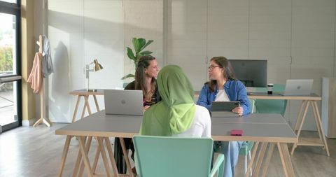 Diverse female coworkers collaborating in bright minimalist office with laptops and tablet