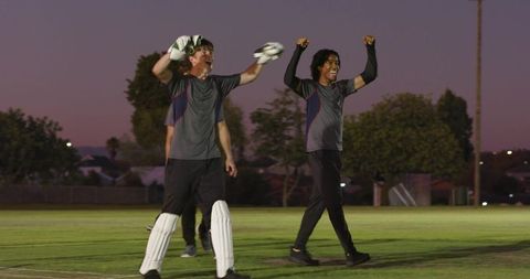 Wicketkeeper celebrating catch at dusk with diverse teammates on cricket field