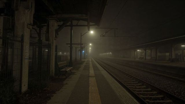Foggy night on deserted railway station platform with glowing lights