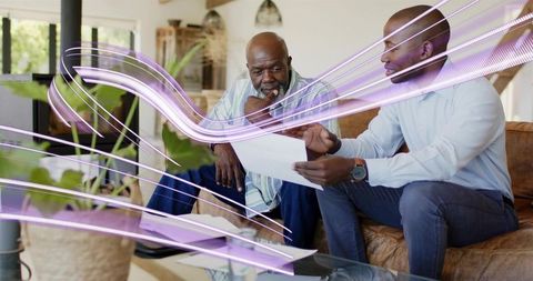 Two men reviewing paperwork on sofa with purple light trails in modern living room