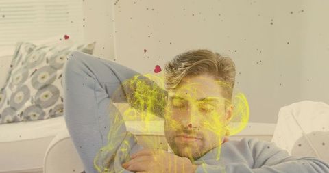 Reclining man in pale blue sweater on sofa with translucent yellow skull and heart overlay