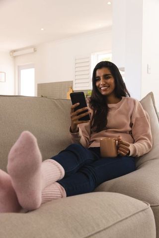 Young Woman Relaxing with Smartphone and Coffee on Cozy Couch