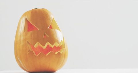 Minimal glowing jack-o-lantern sitting on white tabletop with soft shadow and copy space