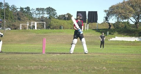 Woman Cricket Batter in Gear Near Pink Stumps on Grassy Field