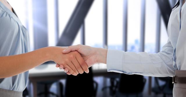 Showcasing collaboration and agreement in business environments, this image is ideal for illustrating themes like successful negotiations, sealing deals, partnership formations, and corporate teamwork. The modern office setting with blurred background highlights professional context and can be used in business presentations, corporate websites, and promotional materials.