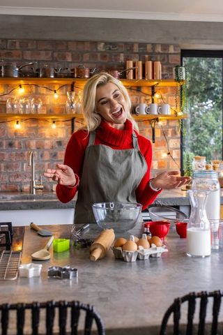 Smiling woman baking in rustic kitchen preparing dough on island with warm lights