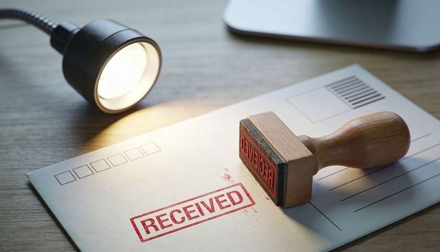 Stamping Received Mail Concept Showing Red RECEIVED Stamp on Envelope under Desk Lamp