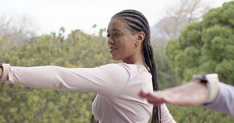Friends stretching on balcony showing braided hair, smartwatch, pink activewear