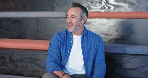 Mature man sitting on tiered wooden benches, wearing blue shirt, looking contemplative