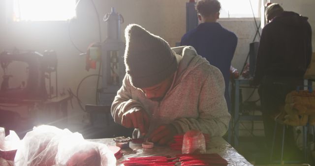 Focused african american man sitting at desk and punching holes, working in clothing workshop. Workshop, small business, work, labor, clothes and production, unaltered.