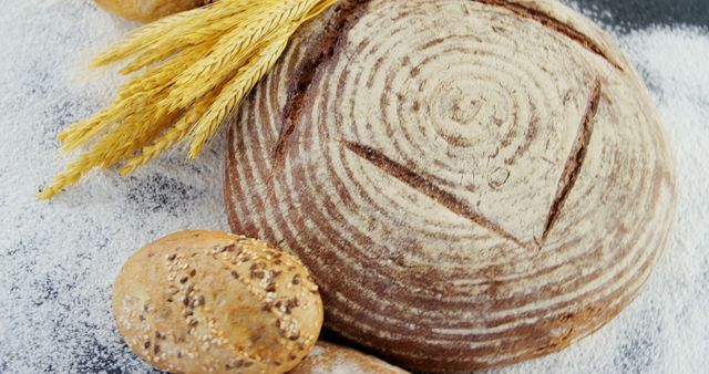 Capturing rustic and wholesome essence, this image showcases freshly baked artisan bread decorated with wheat and dusted with flour. Perfect for use in culinary blogs, bakery advertisements, cookbooks, and healthy eating promotions.