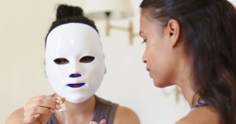 Friends wearing led skincare masks and applying serum during relaxed home beauty routine