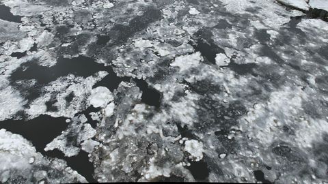 Melting river ice breaking into jagged floes over dark open water during late winter thaw