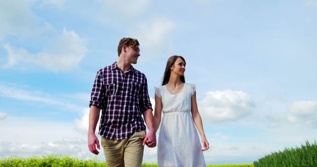 Young couple walking hand in hand down scenic countryside path during bright summer day. Perfect for promoting outdoor activities, romantic getaways, young adult lifestyle, nature retreats, and peaceful rural scenes.