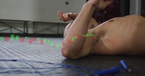 Lying shirtless man raising arm on gym floor with jump rope and candlestick chart