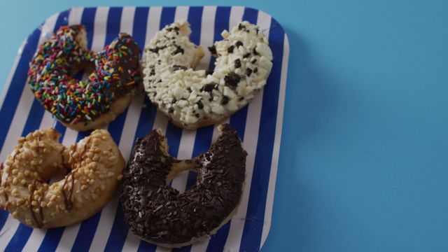 This vibrant and appetizing scene showcases a variety of donuts featuring colorful sprinkles and rich toppings on a striped plate. Perfect for use in blog posts, social media content, advertisements, and other marketing materials related to desserts, celebrations, and indulgent treats.