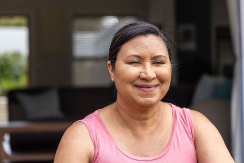 Mature woman smiling and sitting in cozy home wearing pink tank top and stud earrings