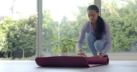 African woman preparing yoga mat in bright home studio, smoothing mat for morning practice