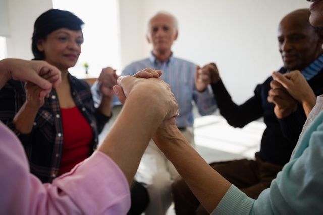 Senior friends sitting in a circle, holding hands, and engaging in a supportive group activity. This image can be used for promoting community events, elderly care services, mental health awareness, and social interaction among senior citizens. It highlights themes of unity, friendship, and emotional support.