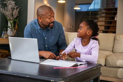 African american father tutoring daughter at home with laptop and notebook