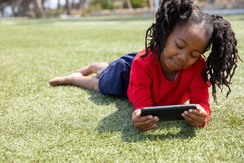 Young Girl Engaged with Tablet on Sunny Green Lawn