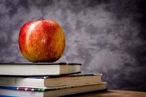 Fresh red apple on stack of books in classroom scene