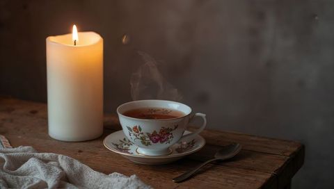 Steaming Floral China Teacup with Lit Candle on Rustic Wooden Table for Cozy Ambience