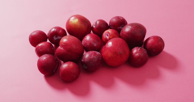 This vibrant display of fresh, whole red plums on a peach-colored background is ideal for use in marketing materials for organic produce, healthy eating blogs, and food photography portfolios. It evokes freshness and health, perfect for advertisements, recipe books, and other nutritional content.