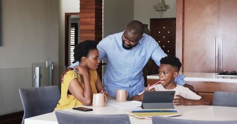 African American family gathering for tablet homework at modern kitchen dining table