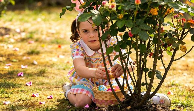 Girl hunting easter eggs in sunny backyard wearing bunny ears and pastel dress