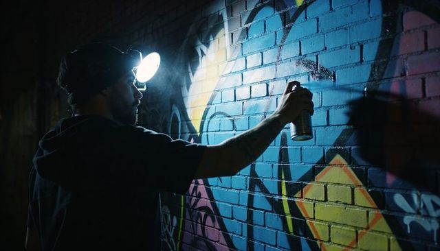 Spraying vivid graffiti mural at night with headlamp and spray can, urban brick wall