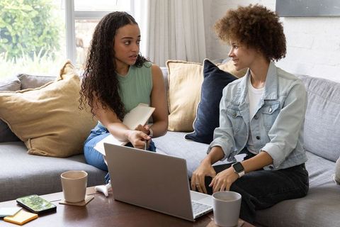 African american women collaborating on laptop discussing notes on cozy living room couch