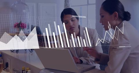Businesswomen Collaborating at Laptop with Futuristic Analytical Graphs