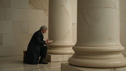Contemplative scholar kneeling in classic hall writing in notebook