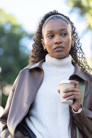 African woman holding coffee cup in leather jacket outdoors thoughtful morning portrait