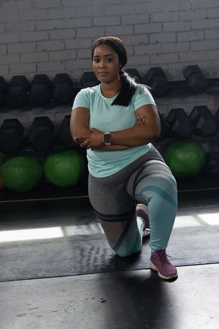 African american woman kneeling stretching in gym wearing light blue activewear